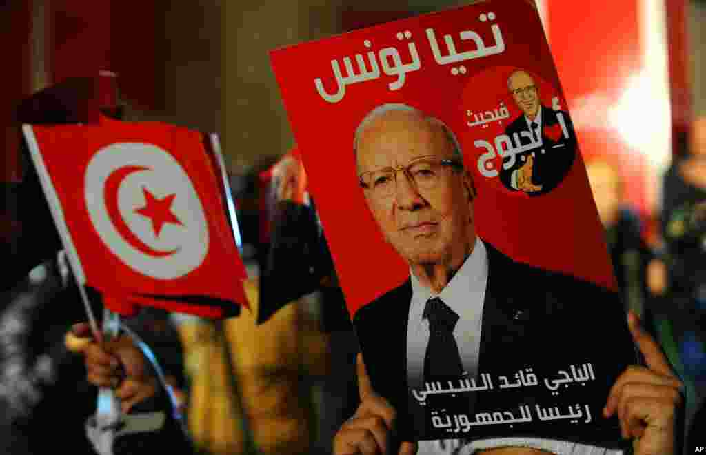 A supporter holds a poster of Tunisian presidential candidate Beji Caid Essebsi as he celebrates after the first results following the second round of the country's presidential election, in Tunis, Sunday, Dec. 21, 2014. 