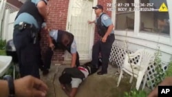 In this frame grab from a body cam provided by the Independent Police Review Authority, Chicago police officers handcuff Paul O'Neal, suspected of stealing a car, after they fired into the vehicle he was driving and then pursued him through a yard.