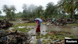 A woman holding an umbrella walks in the rain among debris after a tsunami, in Sumur, Banten province, Indonesia, Dec. 26, 2018. 