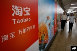 FILE - People walk past an advertising billboard showing the mobile app of Alibaba’s Taobao consumer-to-consumer site at a subway station in Beijing.