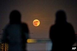 Two Iranian women watch the moon rising over Tehran in Iran, Nov. 14, 2016.