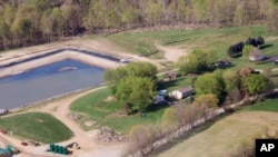 June Chappel’s home in Washington, Pennsylvania, is surrounded by gas drilling: a waste containment pond behind her and gas tanks to the side.