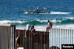 Migrants, part of a caravan of thousands trying to reach the U.S., sit on top of the border fence between Mexico and the United States, in Tijuana, Mexico, Nov. 14, 2018.