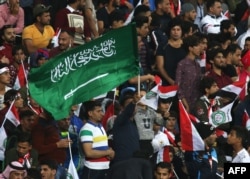 FILE - A football fan waves a Saudi Arabian flag during the friendly football match between Iraq and Saudi Arabia at a city stadium in Basra, Feb. 28, 2018.