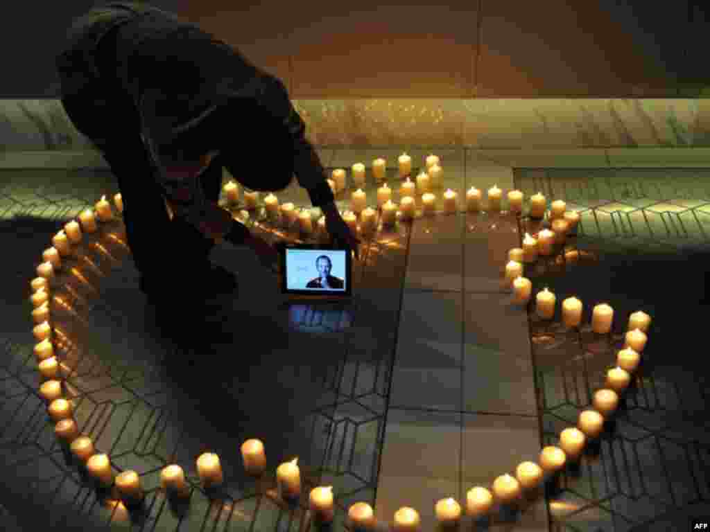 A man places an iPad displaying a picture of Steve Jobs around candles forming the logo of Apple Inc., the company he co-founded, in Chengdu in southwestern China's Sichuan province, on Thursday, Oct. 6, 2011.