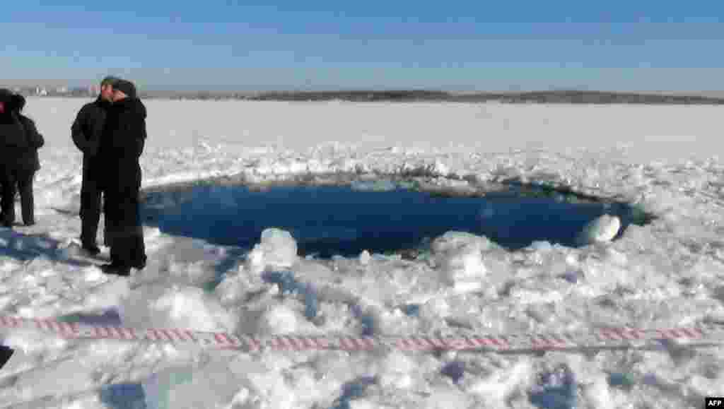 People stand near a six-meter hole in the ice of a frozen lake, the site of a meteor fall, outside the town of Chebakul in the Chelyabinsk region. Photo: Chelyabinsk Region Police Department