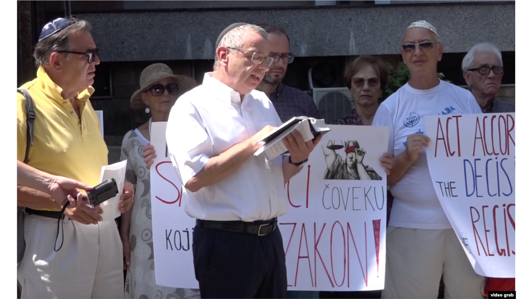 Rabin Isak Asiel čita okupljenima Toru tokom protesta članova jevrejske zajednice ispred Ministarstva pravde zbog odbijanja da se u Registar crkava i verskih zajednica upiše ime novoizabranog predsednika Jevrejske opštine Beograd, Aleksandra Saše Jinkera, u Beogradu, 23. jula 2019.