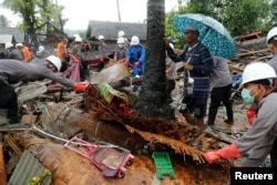 A man holding an umbrella watches as personnel search through the debris of his damaged house after a tsunami, in Sumur, Banten province, Indonesia, Dec. 26, 2018.