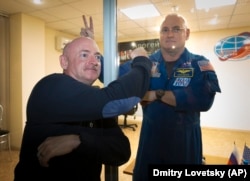 U.S. astronaut Scott Kelly, right, crew member of the mission to the International Space Station, ISS, poses through a safety glass with his brother, Mark Kelly, also an astronaut after a news conference in Russian leased Baikonur cosmodrome, Kazakhstan,