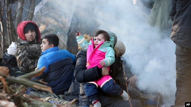 A man carries a child as he gathers with other migrants from the Middle East and elsewhere at the Belarus-Poland border near Grodno Grodno, Belarus, Nov. 9, 2021. (Leonid Shcheglov/BelTA via AP)