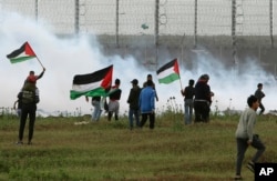 Protesters wave their national flags in front of tear gas fired by Israeli troops near the Gaza Strip border with Israel, on the first anniversary of Gaza border protests east of Gaza City, March 30, 2019.