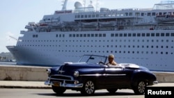 FILE - A man drives his convertible car beside the Maltese-flagged 'Thomson Dream' cruiser docked at Havana's port.