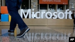 FILE - A man walks past a Microsoft sign set up for the Microsoft BUILD conference at Moscone Center in San Francisco, April 28, 2015. Microsoft says it’s requiring its U.S. suppliers to offer their employees at least 12 weeks paid leave to care for a new