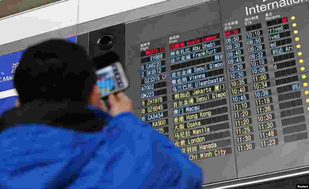 A man takes pictures of a flight information board displaying the Scheduled Time of Arrival (STA) of Malaysia Airlines flight MH370 (top, in red) at the Beijing Capital International Airport in Beijing, China, Mar. 8, 2014.