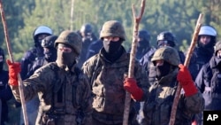 Polish police and border guards stand near barbed wire to stop migrants from the Middle East and elsewhere gathering at the Belarus-Poland border near Grodno, Belarus, Tuesday, Nov. 9, 2021. (Leonid Shcheglov/BelTA via AP)