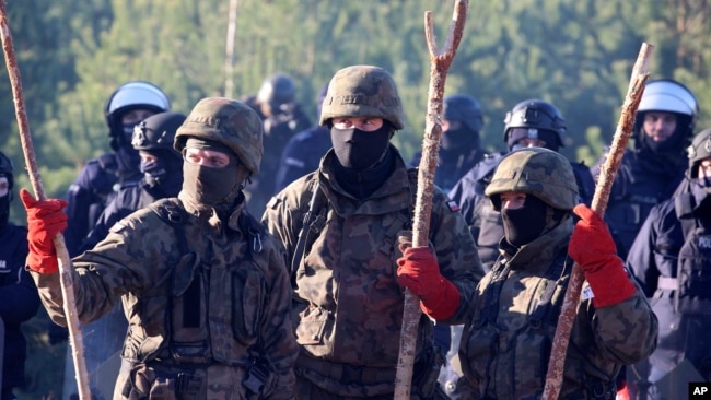 Polish police and border guards stand near barbed wire to stop migrants from the Middle East and elsewhere gathering at the Belarus-Poland border near Grodno, Belarus, Tuesday, Nov. 9, 2021. (Leonid Shcheglov/BelTA via AP)