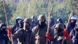 Polish police and border guards stand near barbed wire to stop migrants from the Middle East and elsewhere gathering at the Belarus-Poland border near Grodno, Belarus, Tuesday, Nov. 9, 2021. (Leonid Shcheglov/BelTA via AP)