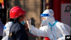 In this photo released by China's Xinhua News Agency, a worker wearing a protective suit collects a throat swab sample at a COVID-19 testing site in Xi'an in northwestern China's Shaanxi Province, Dec. 21, 2021.