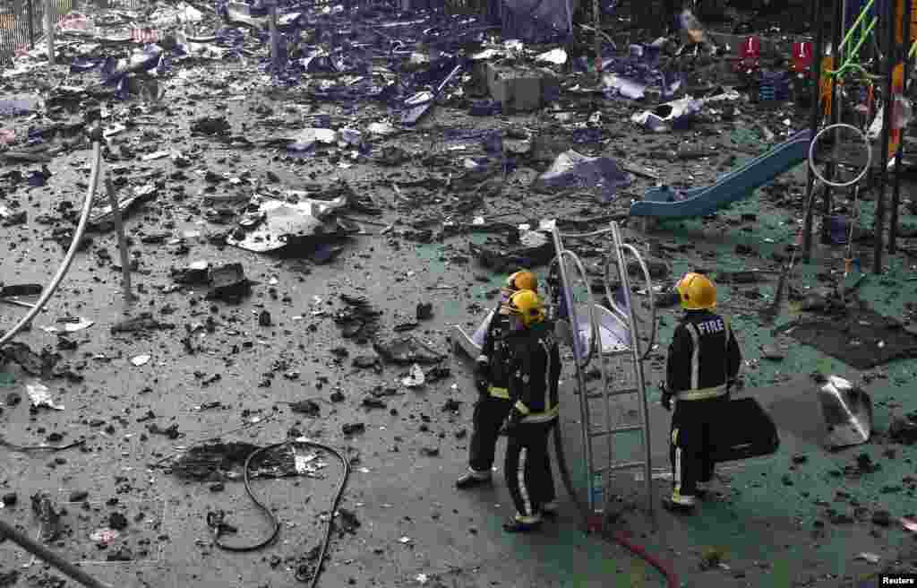 Firefighters stand amid debris in a children's playground near a deadly apartment tower severely damaged by a serious fire, in north Kensington, West London, Britain.
