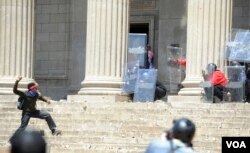 A student, left, hurls a stone at police and private security on the University of the Witwatersrand campus in Johannesburg South Africa on Monday, Oct. 10, 2016. Tear gas and water cannon were fired as hundreds of students protested at the university amid a bitter national dispute with university managers and the government over demonstrators