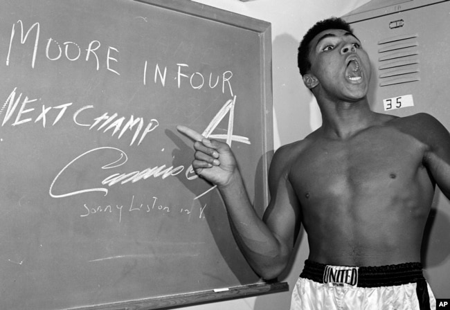 FILE - Young heavyweight boxer Cassius Clay, who later changed his name to Muhammed Ali, points to a sign he wrote on a chalk board in his dressing room before his fight against Archie Moore in Los Angeles, in this Nov. 15, 1962 file photo.