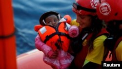 Una tripulante del MV Open Arms, el barco de búsqueda y rescate de Proactiva Open Arms, sostiene a un bebé migrante al pasarlo a una tripulante del MV Aquarius un barco de búsqueda y rescate administrado por SOS Mediterranee y Médicos Sin Fronteras en el mar Mediterráneo frente a las costas de Libia el domingo, 16 de diciembre de 2017. 