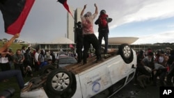 Protesters stand on an overturned car outside Congress where senators later voted in support of a spending cap bill in Brasilia, Tuesday, Nov. 29, 2016.