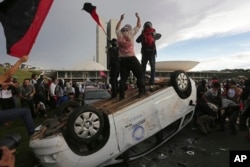 FILE - Protesters stand on an overturned car outside Congress where senators planned to vote on a spending cap bill and the lower Chamber of Deputies was considering controversial anti-corruption legislation, in Brasilia, Brazil, Nov. 29, 2016.
