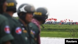 FILE - Cambodian police officers stand guard as Vietnamese people wave their national flags at the Cambodia-Vietnam border in Svay Rieng province, July 19, 2015. 