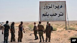 FILE - This photo released on Sept. 3, 2017, by the Syrian official news agency SANA, shows Syrian troops and pro-government gunmen standing next to a placard in Arabic which reads, "Deir el-Zour welcomes you."