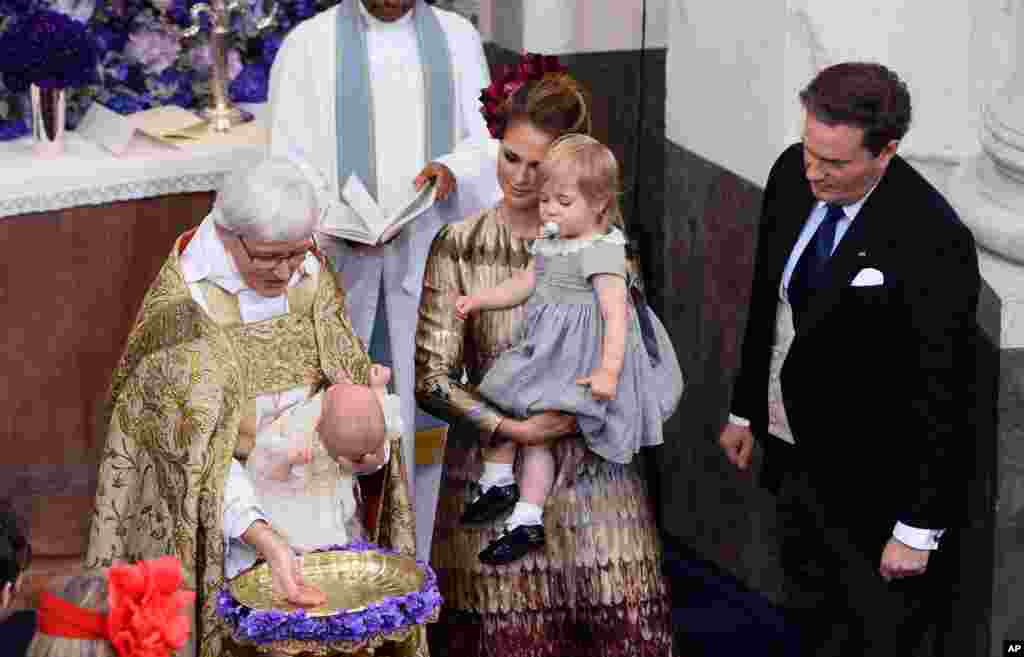 Arch Bishop Antje Jackelen baptizes Sweden&#39;s Prince Nicolas, watched by Princess Madeleine holding Princess Leonore, center, and Christopher O&#39;Neill, during a ceremony, at the Drottningholm Palace Church, near Stockholm.