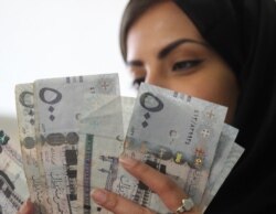 Seorang perempuan Saudi berpose dengan uang kertas riyal Saudi di tempat penukaran mata uang asing di Riyadh, Arab Saudi. (Foto: REUTERS/Faisal Al Nasser)