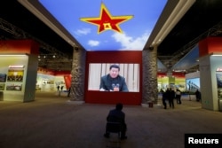 FILE - A visitor watches a video showing Chinese President Xi Jinping at a military meeting during an exhibition displaying China's achievements for the past five years, as a part of the celebrations of the upcoming 19th National Congress of the Communist Party of China.