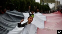 A boy chants slogans through a gap in a national flag raised by Shiite rebels, known as Houthis, during a protest against Saudi-led airstrikes in Sanaa, Yemen, April 15, 2016. 