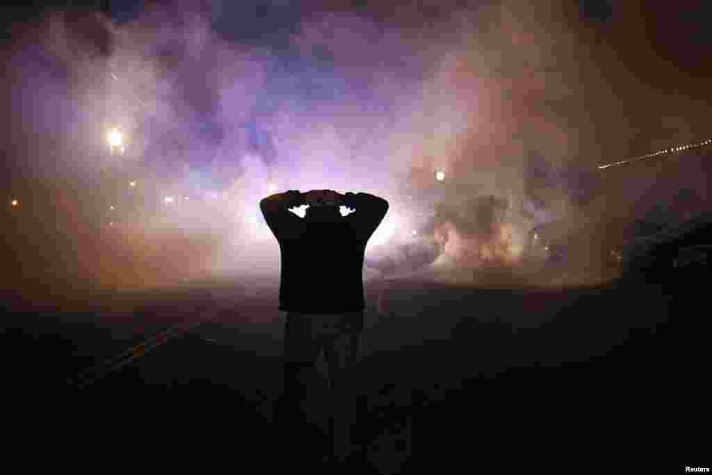 A protester stands with his hands on his head as a cloud of tear gas approaches after a grand jury returned no indictment in the shooting of Michael Brown in Ferguson, Missouri, Nov. 24, 2014. 