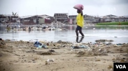 A woman wades near a beach in Monrovia, Liberia. Though poverty does not discriminate, women have fewer resources to cope. (B. Muchler/VOA News)