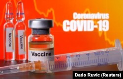 FILE - Small bottles labelled with "Vaccine" stickers seen near a medical syringe in front of displayed "Coronavirus COVID-19" words in this illustration taken April 10, 2020.