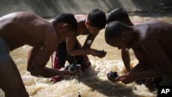 In this Dec. 5, 2017 photo, Angel Villanueva, right, looks for pieces of gold and other valuables in the debris he scooped up from the bottom of the polluted Guaire River, alongside other scavengers, in Caracas, Venezuela. (AP Photo/Ariana Cubillos)