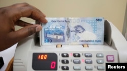 FILE - A cashier counts Qatari riyal notes at a money changer in Doha, May 28, 2013.