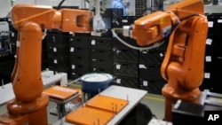 File - A Chinese worker is seen behind orange robot arms at work at Rapoo Technology factory in southern Chinese industrial boomtown of Shenzhen, Aug. 21, 2015.