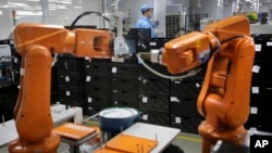 FILe - A Chinese worker is seen behind orange robot arms at work at Rapoo Technology factory in southern Chinese industrial boomtown of Shenzhen, Aug. 21, 2015.