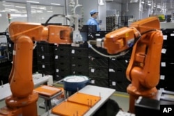 FILE - A Chinese worker is seen behind orange robot arms at work at Rapoo Technology factory in southern Chinese industrial boomtown of Shenzhen, Aug. 21, 2015.