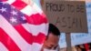 Seorang demonstran berdiri antara bendera AS dan sebuah poster saat unjuk rasa menentang kejahatan kebencian terhadap warga Asia-Amerika di luar balai kota Los Angeles, California, Sabtu, 27 Maret 2021. (Foto: Ringo Chiu/Reuters)