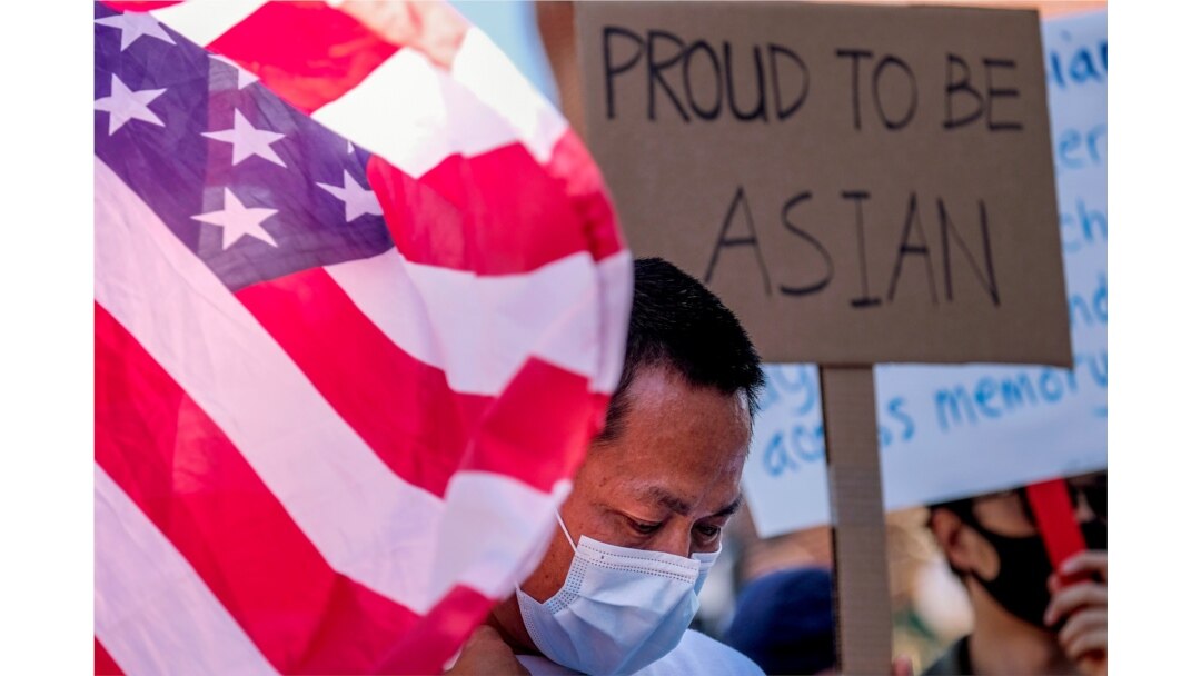 Seorang demonstran berdiri antara bendera AS dan sebuah poster saat unjuk rasa menentang kejahatan kebencian terhdapa warga Asia-Amerika di luar balai kota Los Angeles, California, Sabtu, 27 Maret 2021. (Foto: Ringo Chiu/Reuters)