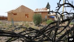 In this Aug. 9, 2018 photo, a burned tree sits in the foreground of Cheri Sharp's new home under construction in Santa Rosa, Calif. After she lost her home in the deadly October 2017 wildfires, Sharp discovered her insurance policy didn't cover the actual cost of rebuilding the house.
