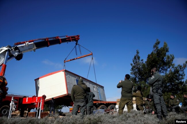 A pre-fabricated home is lowered onto a tow truck as it is removed during an evacuation by Israeli paramilitary police of Jewish settlers from Amona, an illegal outpost in the Israeli-occupied West Bank, Jan. 3, 2019.