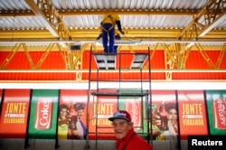 FILE - Workers fix lighting above advertising posters of FIFA sponsors outside a metro station near the World Cup stadium in Sao Paulo.