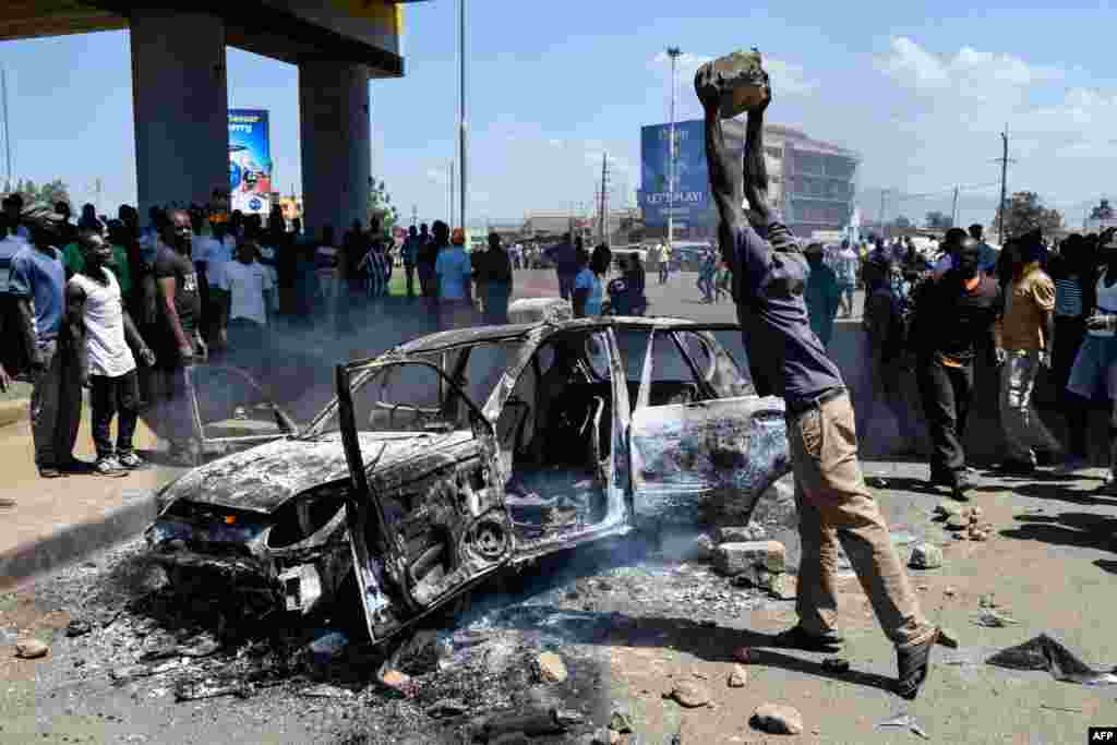 케냐 키수무에서 야당연합(NASA)를 지지하는 시위가 열린 가운데 한 남성이 불 탄 차량에 돌을 던지고 있다.