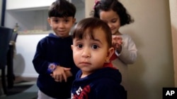 Syrian refugee Mohammad word al Jaddou, front, stands in front of his siblings twins Maria, right, and Hasan at their apartment in Dallas. 