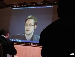FILE- In this Feb. 17, 2016, photo, former National Security Agency contractor Edward Snowden, center, speaks via video conference to people in the Johns Hopkins University auditorium in Baltimore.